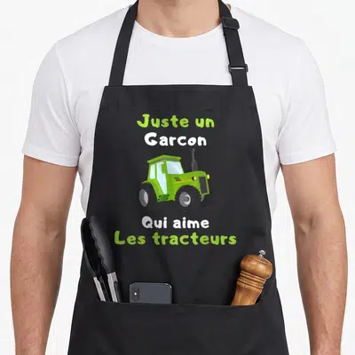 Tablier de cuisine noir avec tracteur vert et texte Juste un Garcon Qui aime Les tracteurs imprimé au centre.
