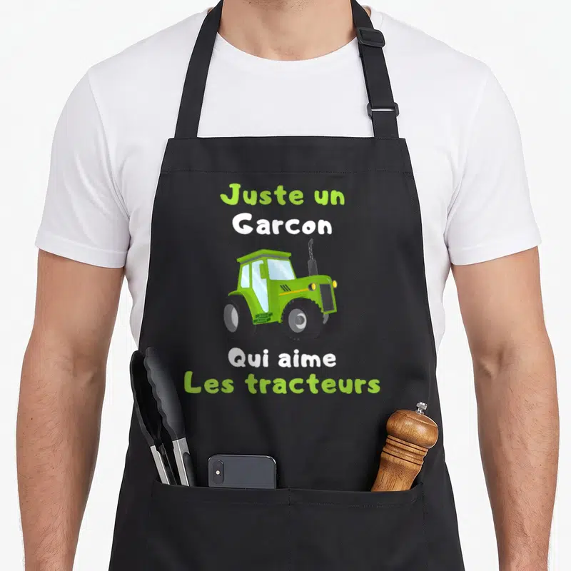 Tablier de cuisine noir avec tracteur vert et texte Juste un Garcon Qui aime Les tracteurs imprimé au centre.