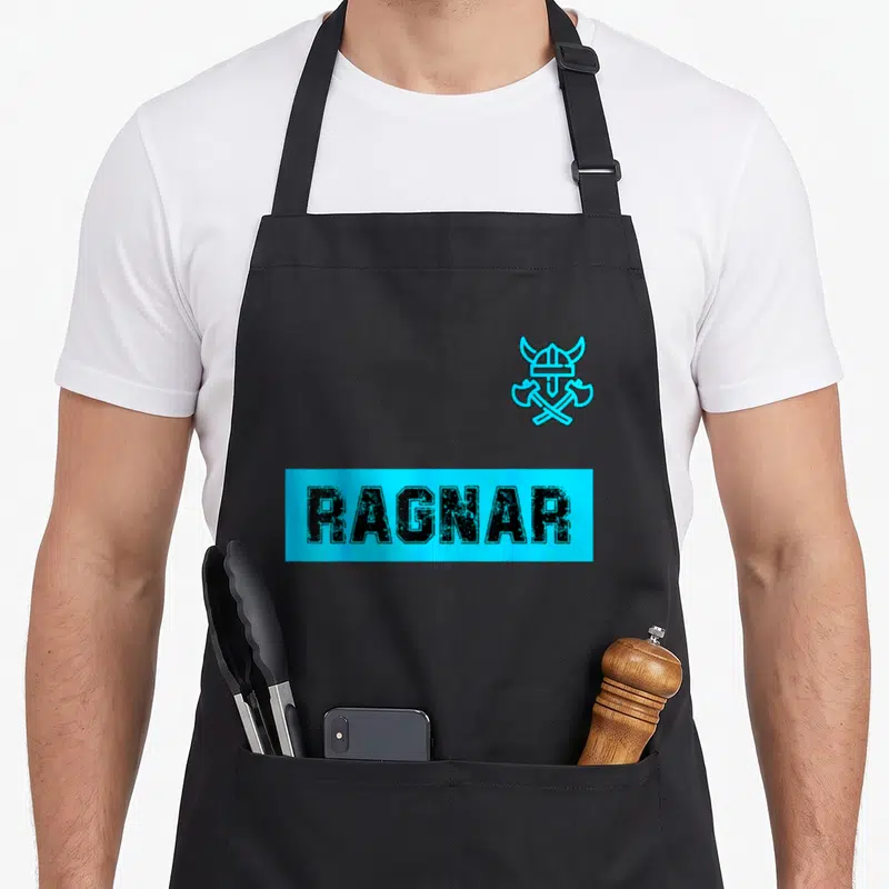 Tablier de cuisine noir avec le mot RAGNAR en cyan et un logo de casque viking surmontant des haches croisées.