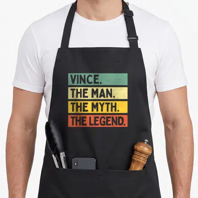 Tablier de cuisine noir avec inscription Vince The Man The Myth The Legend sur bandes colorées vert jaune et orange.