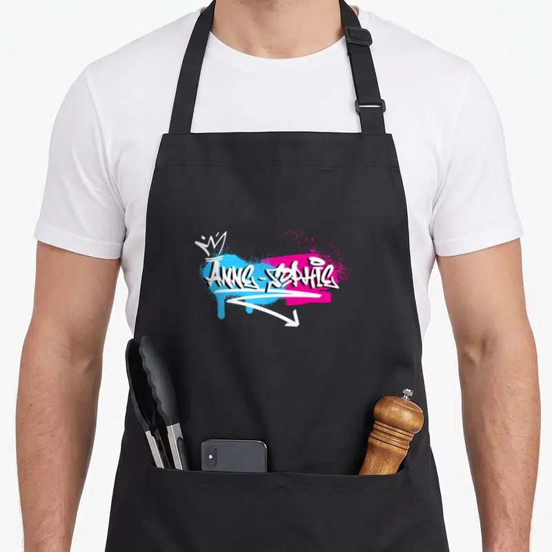 Tablier de cuisine noir avec le prénom Anne-Sophie en style graffiti blanc sur fond bleu et rose vif.