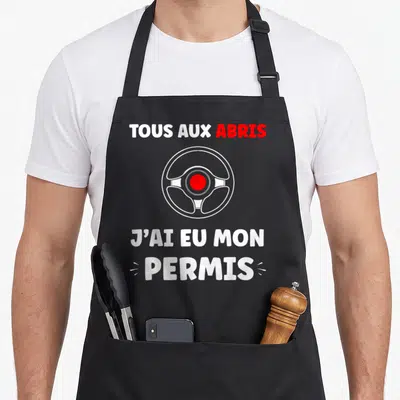 Tablier de cuisine noir avec volant blanc et texte tous aux abris j'ai eu mon permis en blanc et rouge.