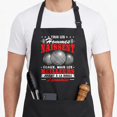 Tablier de cuisine noir avec trois boules de pétanque et texte blanc rouge sur fond gris uni.