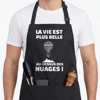Tablier de cuisine noir avec une montgolfière blanche et l'inscription La vie est plus belle au-dessus des nuages.