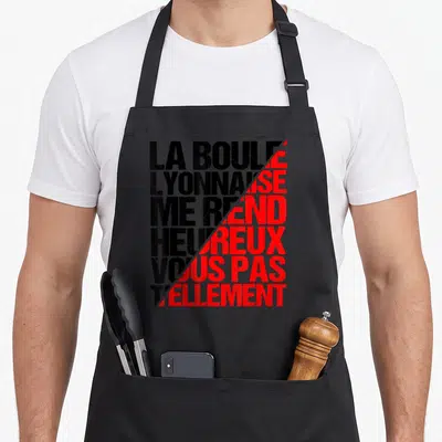 Tablier de cuisine noir avec inscription typographique noire et rouge La boule lyonnaise me rend heureux vous pas tellement.