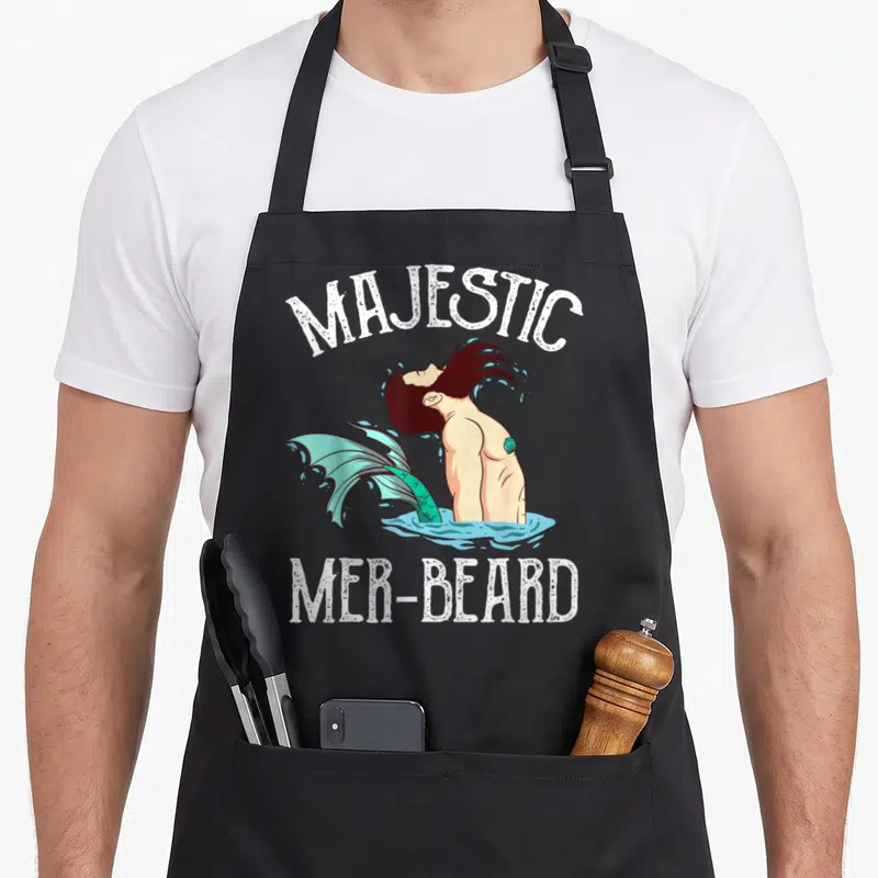 Tablier de cuisine noir avec illustration d'un majestueux mer-beard hipster aux cheveux foncés et queue turquoise émergeant de l'eau.