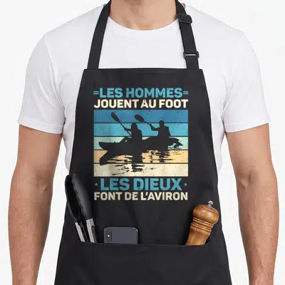 Tablier de cuisine noir avec silhouette de kayaks et texte Les hommes jouent au foot les dieux font de l'aviron.