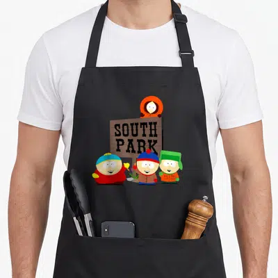 Tablier de cuisine noir avec illustration des quatre personnages devant un panneau en bois indiquant South Park.