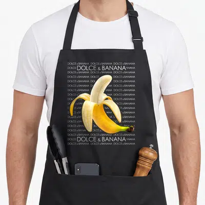 Tablier de cuisine noir avec une banane pelée jaune et le texte Dolce et Banana en arrière-plan blanc.