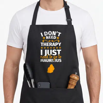 Tablier de cuisine noir avec inscription blanche et orange I don't need therapy I just need to go to Mauritius surmontant une silhouette de l'île.