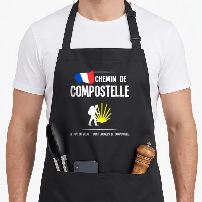 Tablier de cuisine noir avec illustration d'un pèlerin, une coquille jaune et le texte Chemin de Compostelle.
