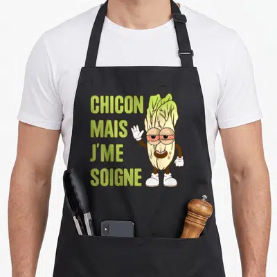 Tablier de cuisine noir avec une endive cartoon aux yeux rouges et le texte chicon mais jme soigne imprimé en vert.