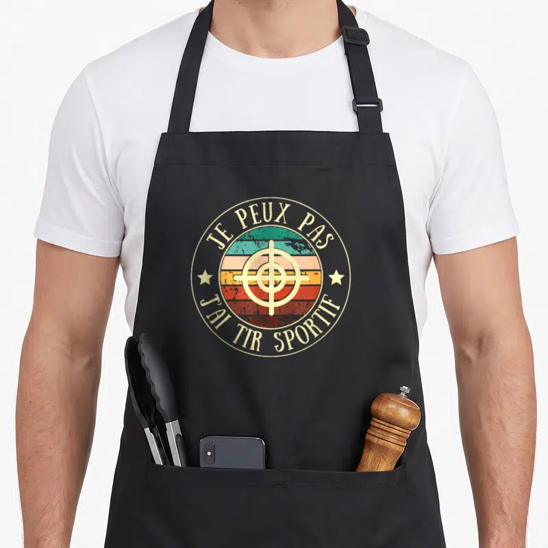 Tablier de cuisine noir avec logo circulaire vintage affichant une cible et le texte je peux pas j'ai tir sportif en lettres dorées.