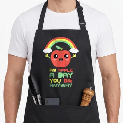 Tablier de cuisine noir avec une pomme souriante sous un arc-en-ciel et le texte An Apple A Day You Die Anyway en lettres colorées.