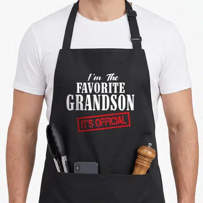 Tablier de cuisine noir avec inscription blanche I'm The Favorite Grandson et tampon rouge It's Official en bas du motif.