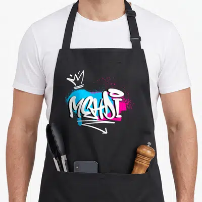 Tablier de cuisine noir avec un graffiti blanc Mehdi sur fond bleu et rose et une petite couronne.