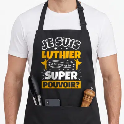 Tablier de cuisine noir avec le texte Je suis luthier et toi quel est ton super pouvoir en orange et blanc.