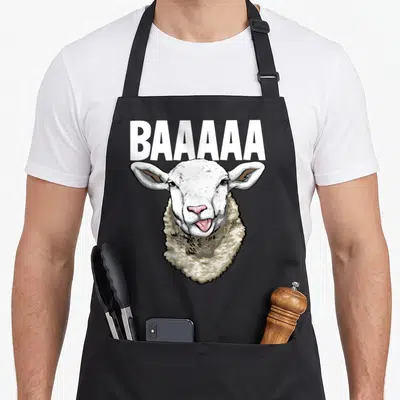 Tablier de cuisine noir avec illustration d'un mouton blanc baveux et texte BAAAAA en lettres capitales blanches au-dessus.