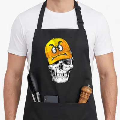 Tablier de cuisine noir avec illustration d'un crâne portant une casquette jaune aux yeux expressifs et à la mine contrariée.