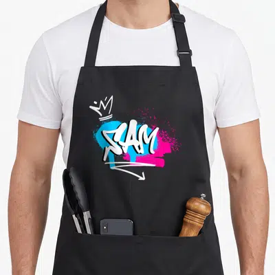 Tablier de cuisine noir avec le prénom Sam en graffiti blanc sur taches bleues et roses et une petite couronne.