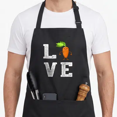 Tablier de cuisine noir avec une carotte orange formant le mot LOVE en lettres blanches texturées.