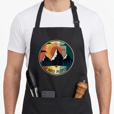 Tablier de cuisine noir avec un motif circulaire représentant des montagnes et le texte « JE DÉTESTE LES GENS » en bas.
