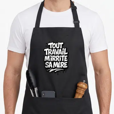 Tablier de cuisine noir avec l'inscription tout travail m'irrite sa mère en lettres blanches style graffiti.