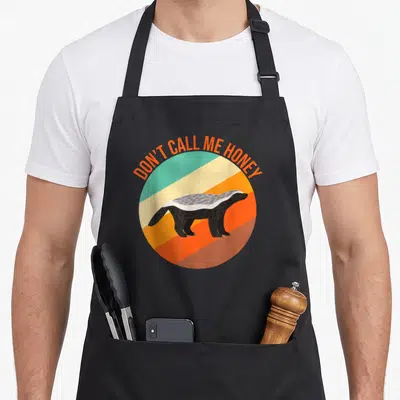 Tablier de cuisine noir avec illustration d'un blaireau honey badger sur un cercle aux couleurs rétro et texte orange.