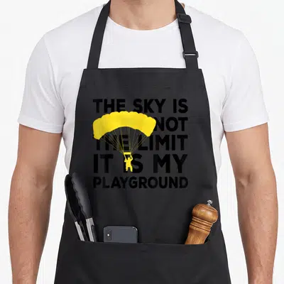Tablier de cuisine noir avec une illustration de parachute jaune et le texte The Sky Is Not The Limit It Is My Playground imprimé en noir.