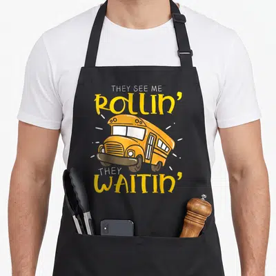 Tablier de cuisine noir avec illustration de car jaune et texte They See Me Rollin They Waitin imprimé en jaune et blanc.