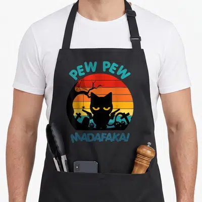 Tablier de cuisine noir avec un chat noir tenant deux revolvers devant un soleil couchant rétro.