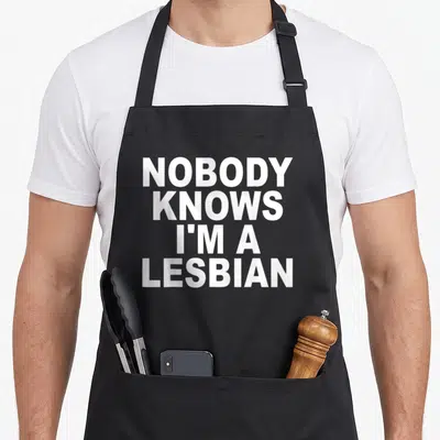 Tablier de cuisine noir avec le texte blanc Nobody Knows I'm A Lesbian imprimé en grandes lettres capitales au centre.