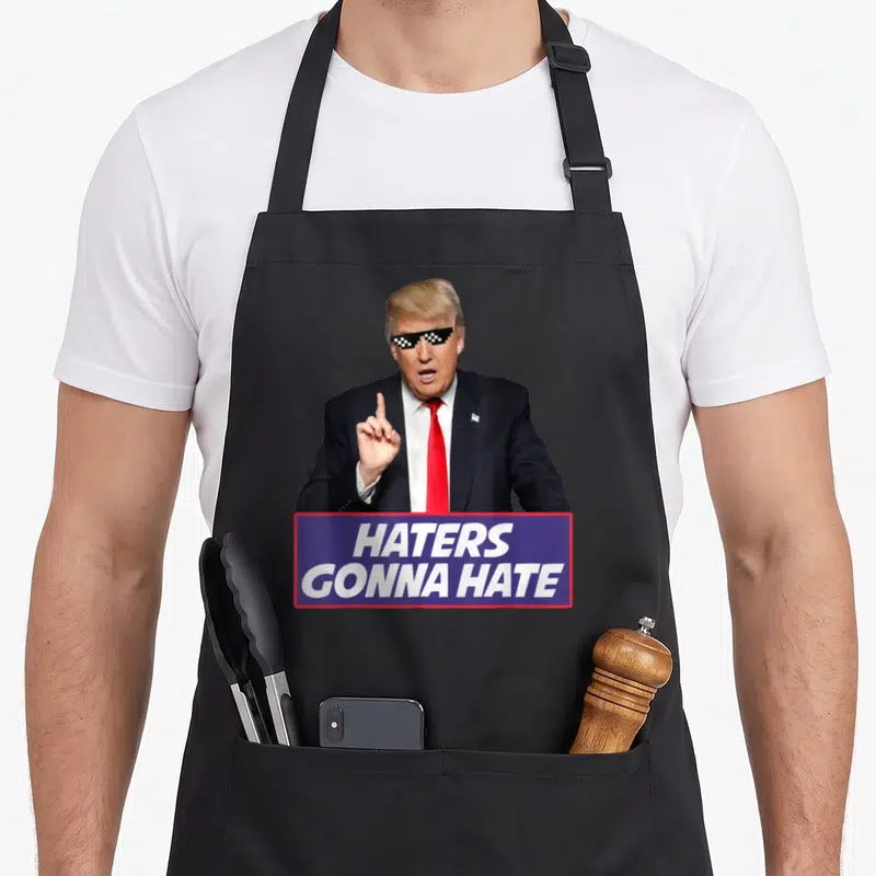 Tablier de cuisine noir avec personnage en costume rouge et lunettes pixelisées sous le texte Haters Gonna Hate.