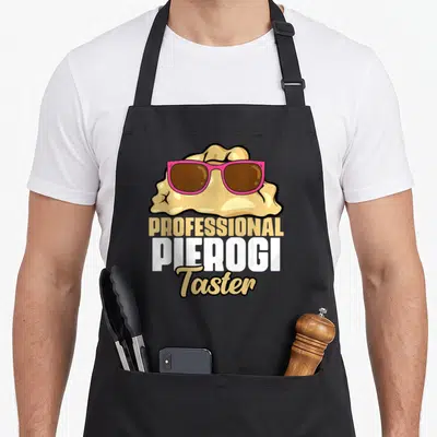 Tablier de cuisine noir avec un pierogi portant des lunettes roses et le texte Professional Pierogi Taster imprimé en lettres jaunes, blanches et dorées.