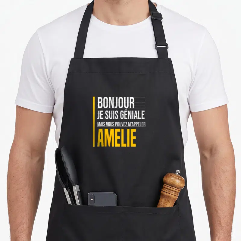 Tablier de cuisine noir avec le texte Bonjour je suis géniale mais vous pouvez m'appeler Amelie en blanc et jaune.