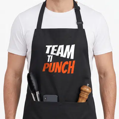 Tablier de cuisine noir avec le texte team ti punch en blanc et orange sur fond uni.