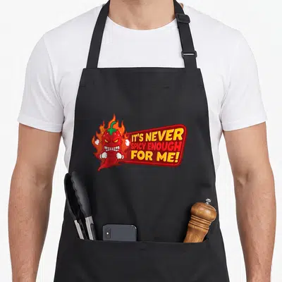 Tablier de cuisine noir avec illustration d'un piment rouge en feu et texte It's never spicy enough for me.