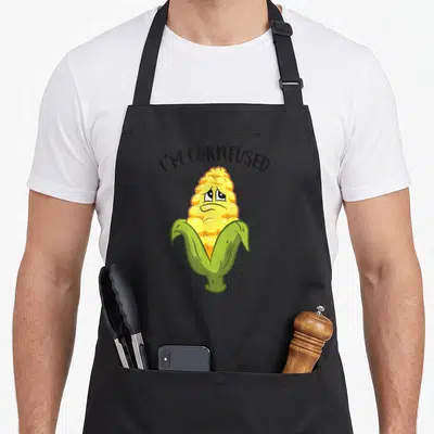 Tablier de cuisine noir avec un épi de maïs aux yeux tristes et le texte I'M CORNFUSED au-dessus.