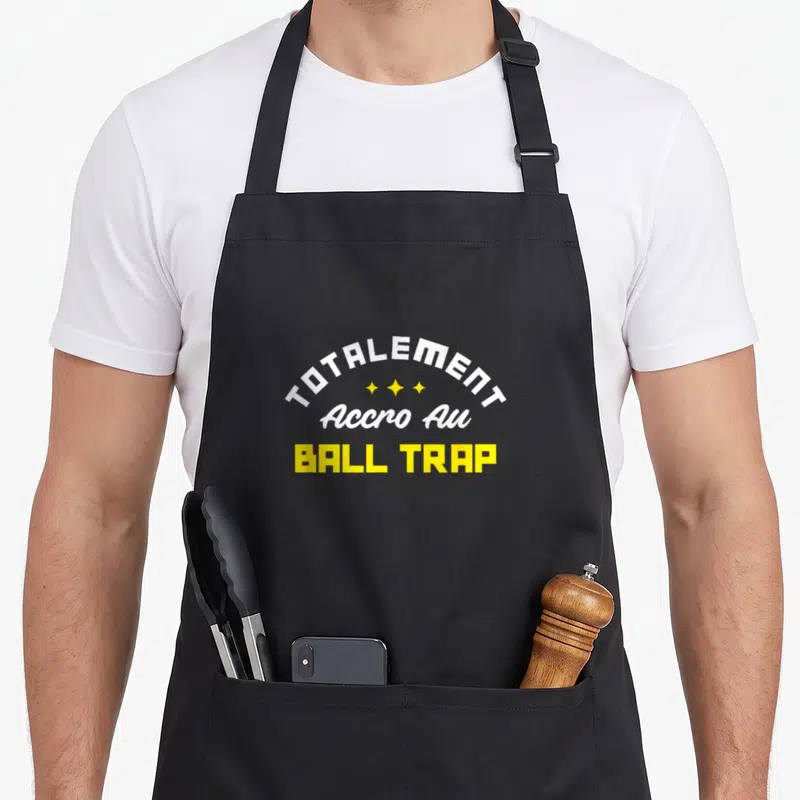Tablier de cuisine noir avec l'inscription totalement accro au ball trap en blanc et jaune.