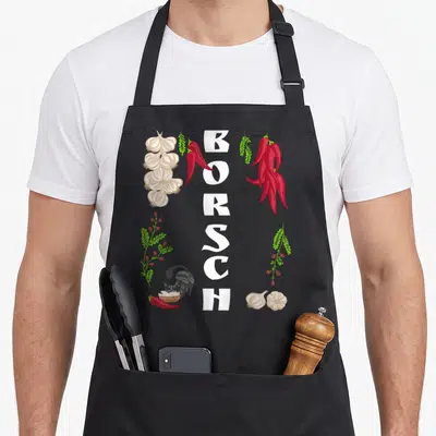 Tablier de cuisine noir avec le mot BORSCH vertical, un chat en vêtement traditionnel, ail et piments rouges.