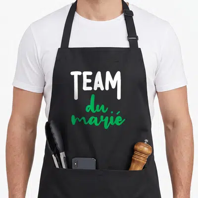 Tablier de cuisine noir avec l'inscription TEAM du marié en lettres blanches et vertes