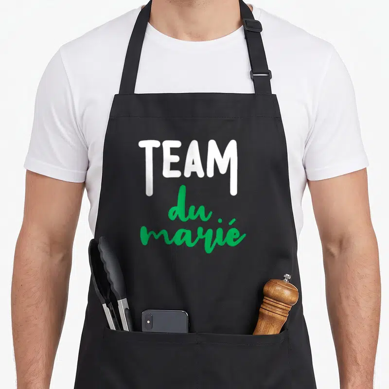 Tablier de cuisine noir avec l'inscription TEAM du marié en lettres blanches et vertes