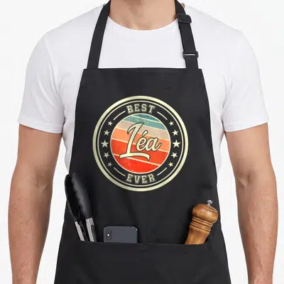 Tablier de cuisine noir avec logo circulaire vintage affichant le prénom Léa Best Ever entouré d'étoiles.