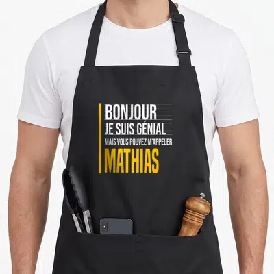 Tablier de cuisine noir avec le texte Bonjour je suis génial mais vous pouvez m'appeler Mathias en blanc et jaune.