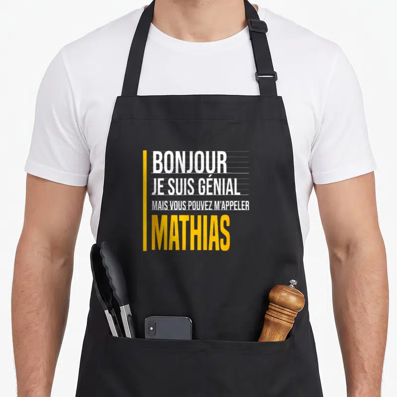 Tablier de cuisine noir avec le texte Bonjour je suis génial mais vous pouvez m'appeler Mathias en blanc et jaune.