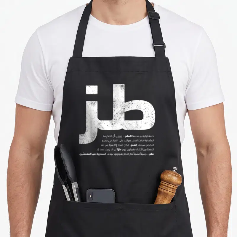 Tablier de cuisine noir avec grand motif blanc en calligraphie arabe et bloc de texte explicatif en dessous.