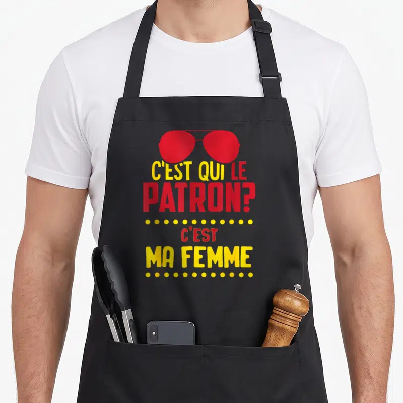 Tablier de cuisine noir avec inscription rouge et jaune C'est qui le patron c'est ma femme sous des lunettes de soleil rouges