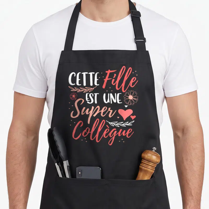 Tablier de cuisine noir avec le texte Cette Fille Est Une Super Collègue en rose et blanc entouré de cœurs et de fleurs.