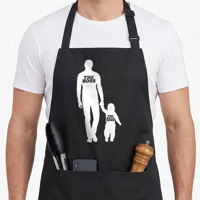 Tablier de cuisine noir avec silhouettes parent et enfant portant des inscriptions humoristiques en anglais.