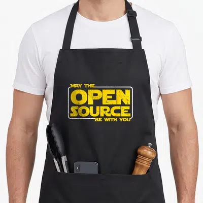 Tablier de cuisine noir avec l'inscription jaune May the Open Source Be with You dans un cadre blanc rectangulaire.
